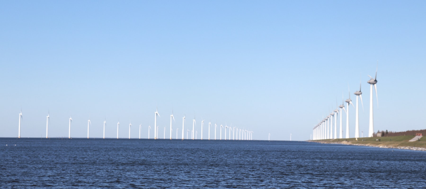A long row of wind turbines running along a coastline and out over open water