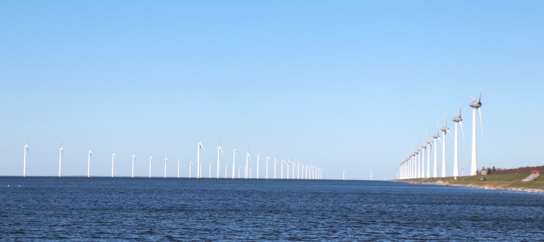 A long row of wind turbines running along a coastline and out over open water